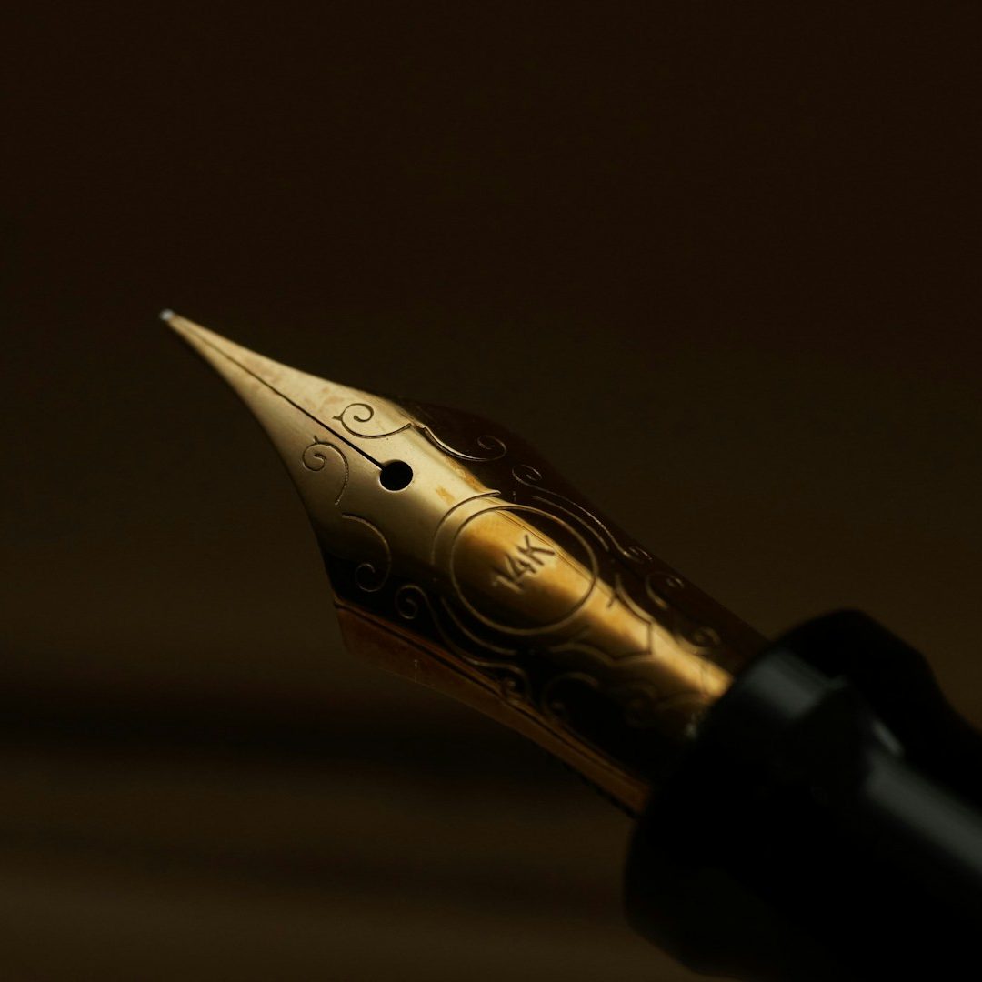 Fountain Pen Image Close-up of a bid writer's gold fountain pen nib on a dark background.